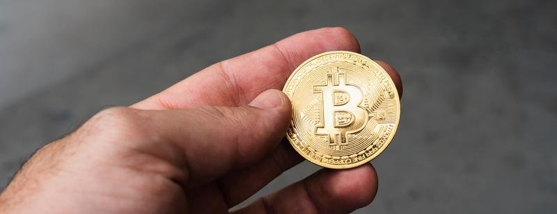 Moneda física que representa un bitcoin sostenida entre los dedos