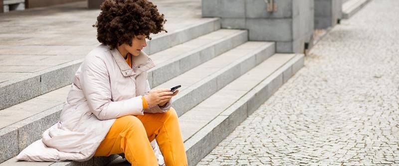 Mujer joven sentada en unas escaleras consultando su teléfono móvil